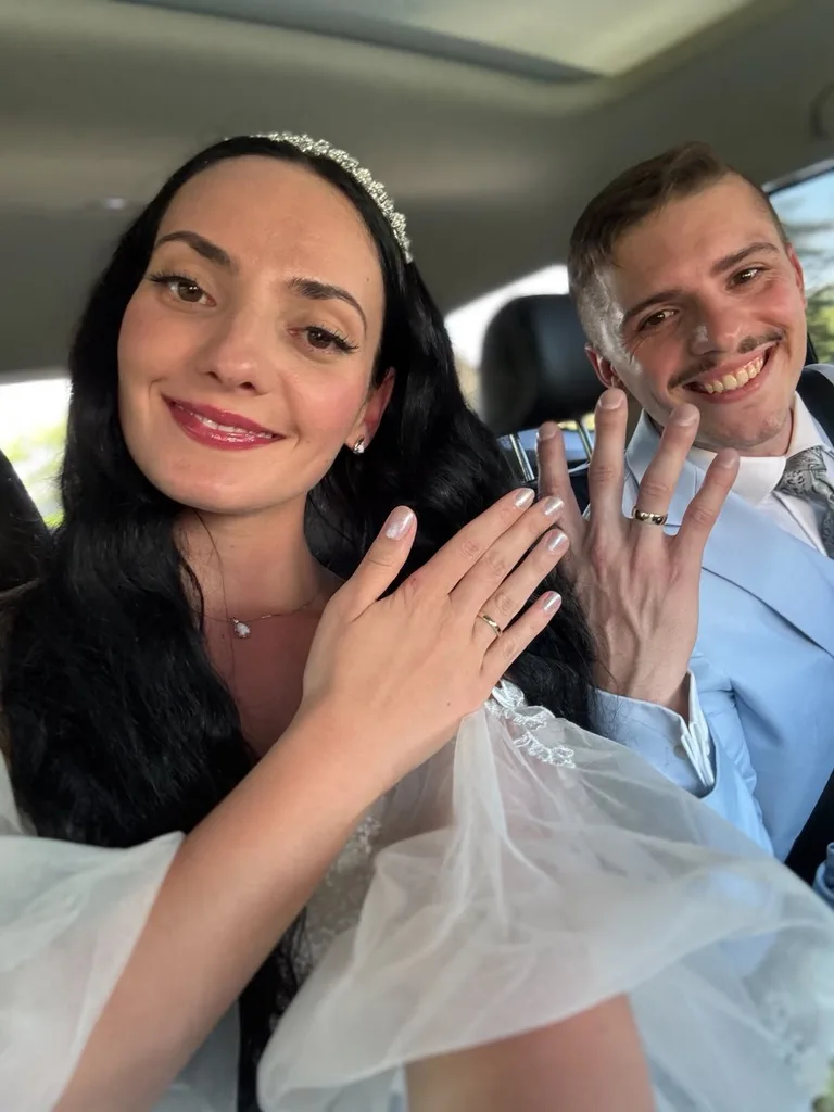 Alice und Pascal zeigen lächelnd ihre Eheringe in die Kamera.